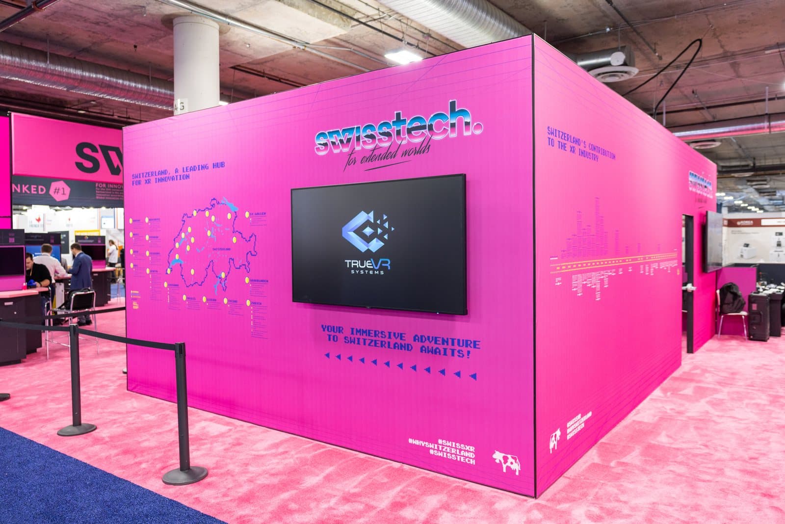 A pink exhibition booth with a screen showing the trueVR systems logo